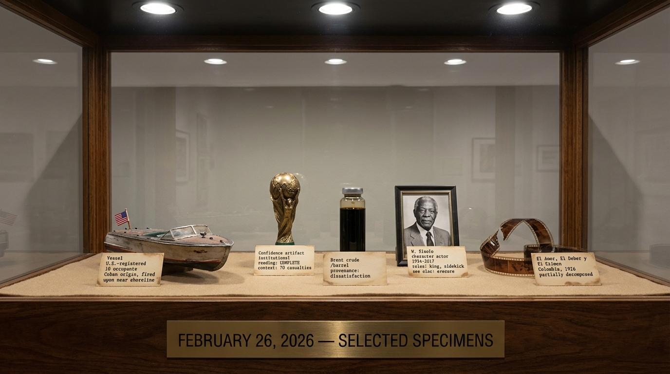 A museum display case behind glass. On sand-colored felt: a model speedboat with an American flag, a FIFA World Cup trophy labeled 'Confidence artifact, institutional, reading: COMPLETE, context: 70 casualties,' a vial of dark crude oil, a framed portrait of a dignified older Black man labeled 'W. Sixolo, character actor, 1934-2017, roles: king, sidekick, see also: erasure,' and a curling strip of film. Brass placard reads: FEBRUARY 26, 2026 — SELECTED SPECIMENS.